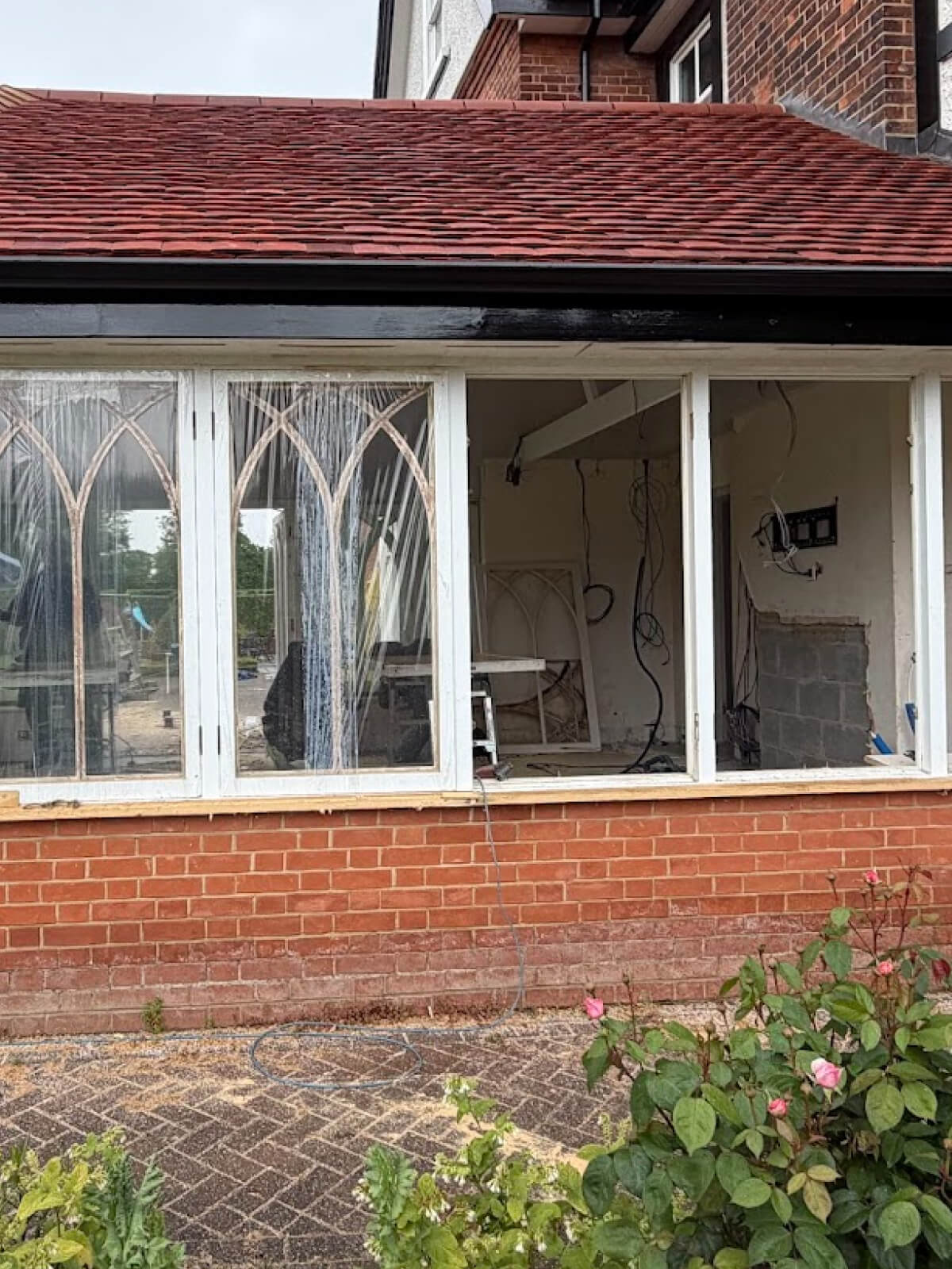 A brick house with large sash windows under renovation in Cambridge; interior walls are exposed, wires hang loose, and furniture is moved aside for sash windows repair.